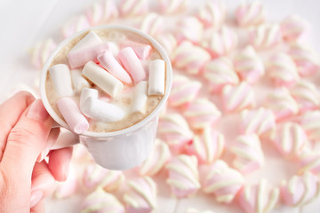cappuccino with marshmallows in the female hand on the background of marshmallows out of focus