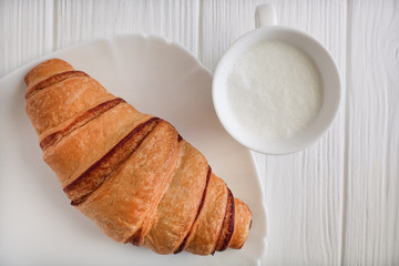 croissant on white wooden background with cappuccino or milk close-up. Top view