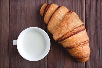 fresh croissant on a wooden table with a cup of milk or cappuccino, top view