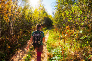 girl with a backpack walk on a forest path in the morning light