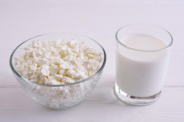 Fresh cottage cheese in a transparent bowl with a glass of milk on a white wooden background