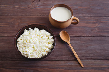 bowl of cottage cheese with a cup of milk with a wooden spoon on a brown table