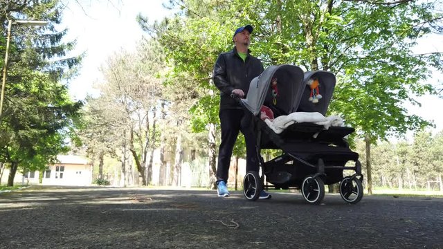Young active father with kids in double stroller in a park.  Man pushing twins stroller, pram.
