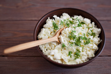 wooden spoon in a bowl with cottage cheese and dill on a brown wooden table background