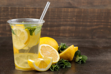 Fototapeta Homemade lemonade with mint and lemon in plastic glasses on a brown background. Refreshing lemonade drink. obraz