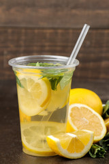 Homemade lemonade with mint and lemon in plastic glasses on a brown background. Refreshing lemonade drink.
