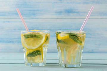 Homemade lemonade with mint and lemon in plastic glasses on a blue wooden background. Refreshing lemonade drink.