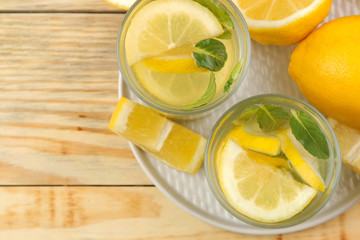 Homemade lemonade with mint and lemon in plastic glasses on a natural wooden background. Refreshing lemonade drink. top view