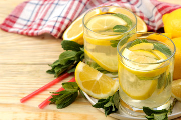 Homemade lemonade with mint and lemon in plastic glasses on a natural wooden background. Refreshing lemonade drink.