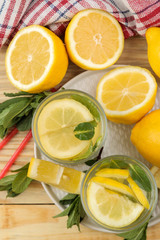 Fototapeta na wymiar Homemade lemonade with mint and lemon in plastic glasses on a natural wooden background. Refreshing lemonade drink. top view