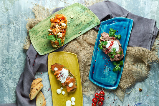 Assorted bruschets on colorful plates. Beautiful serving dishes. Light gray background. Restaurant menu