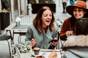 .Group of young friends drinking coffee with cakes in an outdoor cafe in Porto, Portugal. Talking...