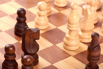 Close-up view of chess game with white and black log pieces on brown chessboard. Fight with horse and pawns.