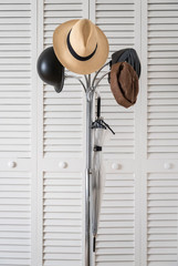 Perchero metálico sobre el que están colgados sombrero Panamá, cascos bici, gorro y paraguas sobre un fondo de puertas blancas con lamas