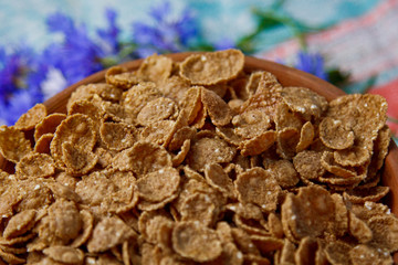 Obraz premium Sugarcorn flakes in a ceramic bowl closeup top view. light breakfast scattered on the table with blue flowers closeup. food fast cooking. healthy food, diet