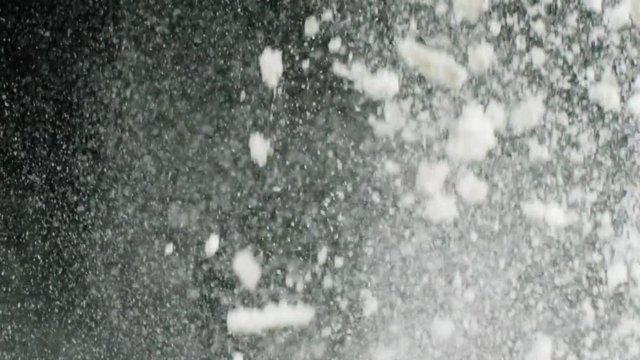 Close-up view of white flakes of powder flying on the black background. Stock footage. Contrast of white and black
