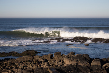 Waves crashing on rocks on Atlantic Ocean beach. Scenic seascape. Beautiful surf at seaside. Splashing waves with foam. Travel and vacation on shore. Rocky coastline. Nature power.