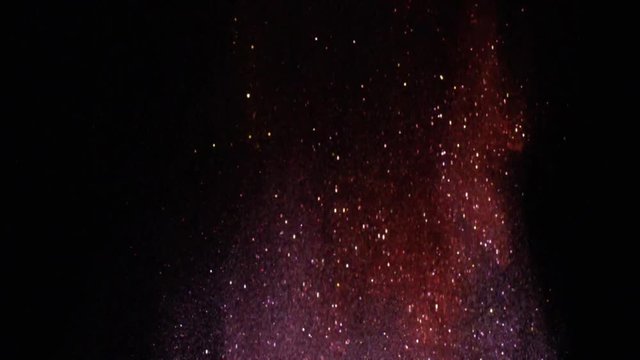 Close-up of sparkling colorful particles flying on the black background and shimmering in the dark. Stock footage. Beautiful view in the dark