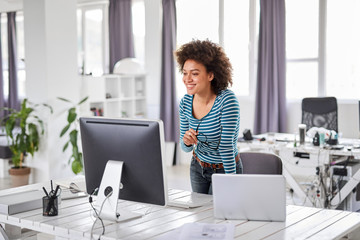 Beautiful mixed race businessoman dressed casual standing in office and looking at computer monitor.