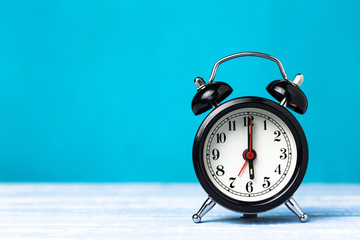 Retro black alarm clock on blue background with copy space. Alarm at 7 clock hand at 6