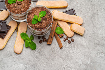 Classic tiramisu dessert in a glass and savoiardi cookies on concrete background