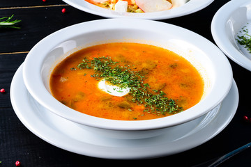 Traditional Russian soup Solyanka cooked with meat, sausages, salted cucumbers and olives. White casserole on the wooden table.