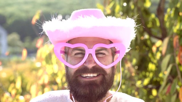 Emotion man with funny hipster pink sunglasses and comic pink hat. Bearded crazy man looking at the camera. Make funny face. Cowboy concept.