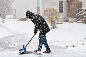 Man abstract in winter coat cleaning shoveling driveway street from snow in heavy snowing snowstorm holding shovel by residential house