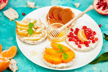 Rice Crisp bread healthy snack with tropical fruit - pomegranate, tangerine, persimmon, apple. Easy breakfast close-up on a blue background. Summer vegan, diet, organic natural food. Copy space.