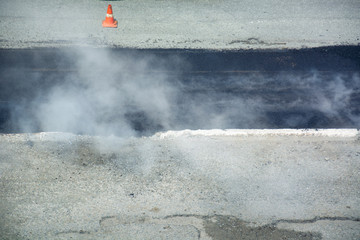 Steam is rising up above the fresh asphalt. Recently paved section of road.