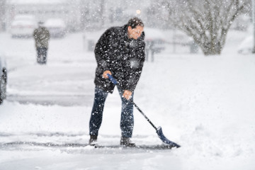 Man in winter coat cleaning shoveling driveway street in heavy snow storm with shovel and abstract...