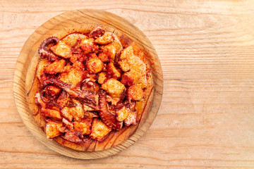 Pulpo a la gallega, an octopus with potatoes and paprika, a typical Spanish Galician dish, on a traditional wooden plate, shot from above on a wooden background with copy space