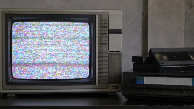 Old TV with signal bad interference, video player and video cassettes on the table