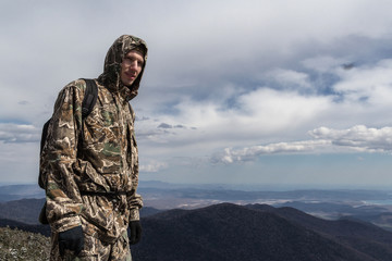 Man in camo clothes and hood, with backpack somewhere on mountains. Maybe soldier or a scout or a...