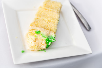 Restaurant or wedding reception white table tablecloth one plate with vanilla cream cake slice closeup and green food coloring