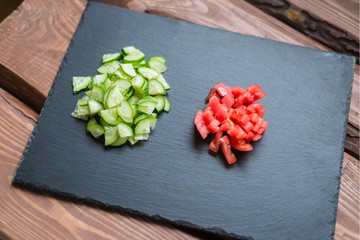 Sliced fresh cucumbers and tomatoes on a black background. Cooking salad from vegetables. The concept of healthy eating, vegetarianism.