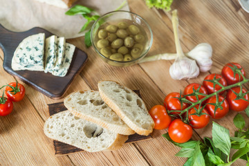 Ingredients for cooking bruschetta: chopped ciabatta, olives, tomatoes, blue cheese on a wooden background. Cooking healthy and tasty food.