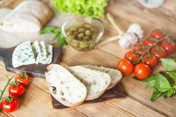 Ingredients for cooking bruschetta: chopped ciabatta, olives, tomatoes, blue cheese on a wooden background. Cooking healthy and tasty food.