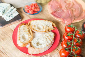 Toasted ciabatta slices and ingredients for making bruschetta on a wooden background.