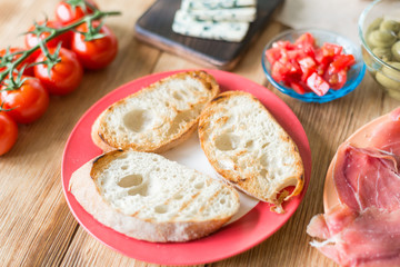 Toasted ciabatta slices and ingredients for making bruschetta on a wooden background.