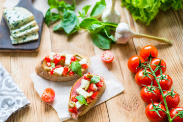 Traditional Italian bruschetta with blue cheese, feta, tomatoes, basil leaves, jamon on a wooden background.