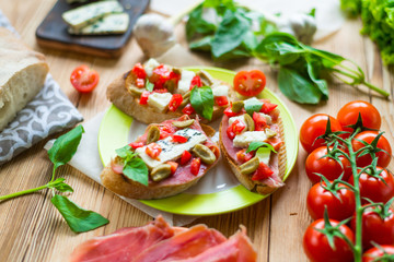Traditional Italian bruschetta with blue cheese, feta, tomatoes, basil leaves, jamon on a wooden background.