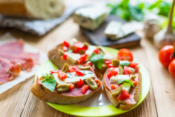 Traditional Italian bruschetta with blue cheese, feta, tomatoes, basil leaves, jamon on a wooden background.