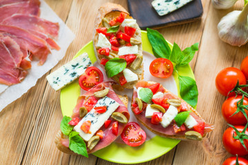 Traditional Italian bruschetta with blue cheese, feta, tomatoes, basil leaves, jamon on a wooden background.