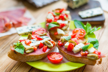 Traditional Italian bruschetta with blue cheese, feta, tomatoes, basil leaves, jamon on a wooden background.