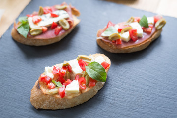 Traditional Italian bruschetta with blue cheese, feta, tomatoes, basil leaves, jamon on black stone background.