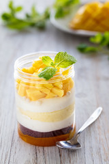 Sweet homemade Mango dessert, cheesecake, trifle, mouse in a glass jar on a light wooden background, vertical composition