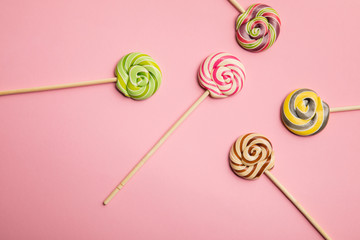 top view of delicious colorful swirl lollipops on wooden sticks on pink background