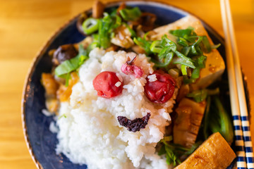 Traditional japanese dish plate in restaurant with wooden table and vegetable dish with shiso, umeboshi and tofu with green onion negi and chopsticks making smiley face