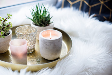 Obraz na płótnie Canvas Cozy real home decoration, burning candles on golden tray with pillow on white faux fur on windowsill